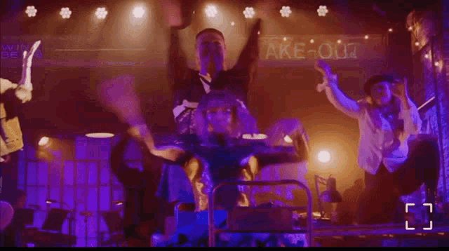 a group of people dancing on a stage in front of a sign that says take-out