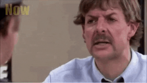 a man with a mustache is talking to another man in a blue shirt and tie .