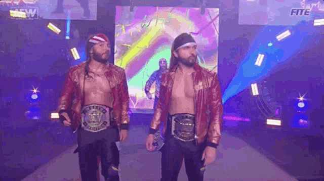 two wrestlers with championship belts are walking down a ramp in a dark room .