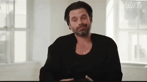 a man with a beard is sitting at a table with his eyes closed and making a funny face .