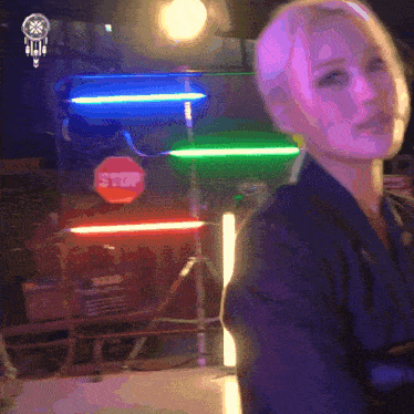 a woman is standing in front of a neon sign that says stop