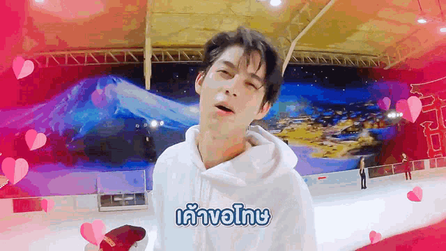 a man in a white hoodie is standing on a ice rink with hearts surrounding him
