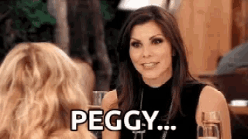 a woman is sitting at a table talking to another woman while holding a glass of champagne .