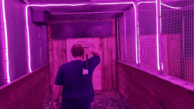 a man throws an axe at a target in a cage with purple lights