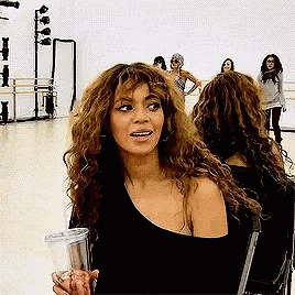a woman with curly hair is sitting in a chair holding a drink