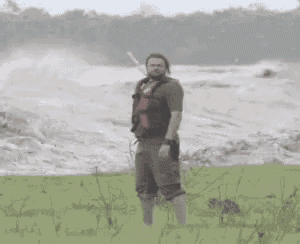 a man is standing on a beach with his arms outstretched in front of a large wave .