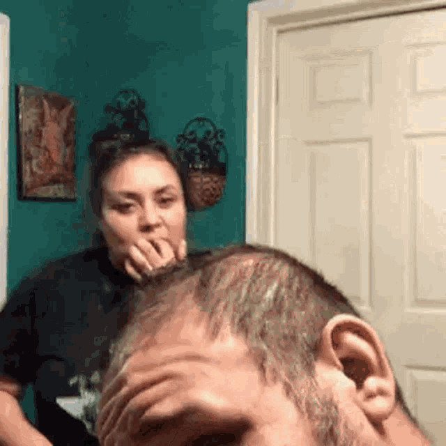 a woman is covering her mouth while looking at a man 's head in a room .