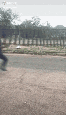 a person is walking down a street with a fence in the background .