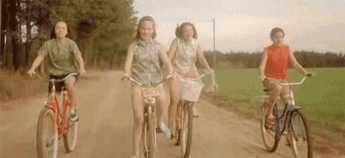 a group of young women are riding bikes down a dirt road .