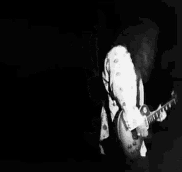 a black and white photo of a man playing a guitar on a stage .