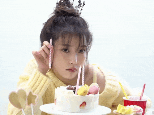 a woman with a crown on her head looks at a birthday cake with candles