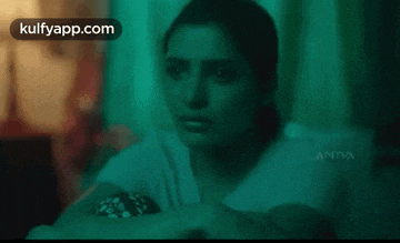 a woman is sitting on a couch in a dark room looking at something .