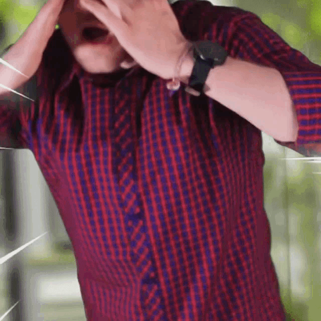 a man wearing a watch and a plaid shirt covers his face with his hands