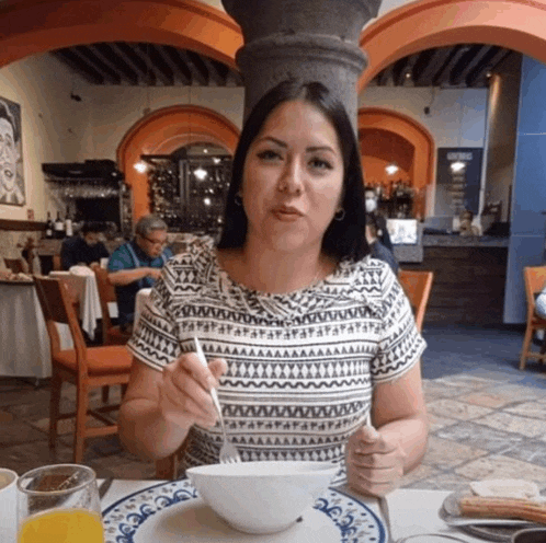 a woman is sitting at a table with a bowl of food in front of her