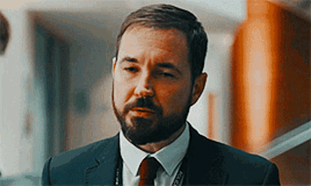 a man with a beard is wearing a suit and tie and a lanyard with the word police on it .