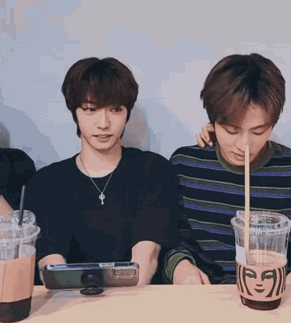 two young men sitting at a table with a starbucks cup