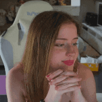 a woman is sitting in a white chair with her hands folded and looking at the camera .