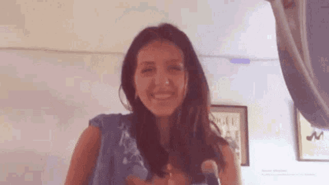 a woman in a blue shirt is smiling while holding a brush in her hand .