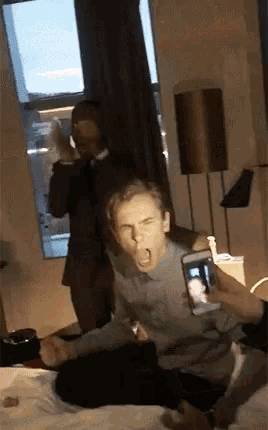 a man sitting on a bed taking a selfie with a cell phone