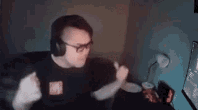 a man wearing headphones and glasses is dancing in front of a computer monitor .