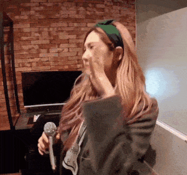 a woman wearing a green headband is singing into a microphone .