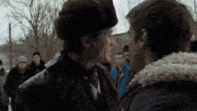 two men are standing next to each other in front of a crowd . one of the men is wearing a fur hat .