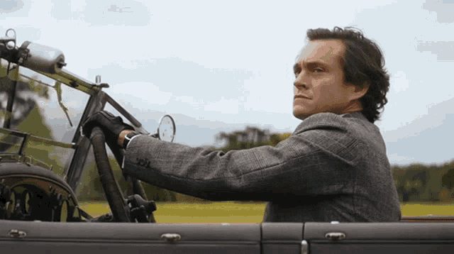 a man in a suit and gloves is driving a car