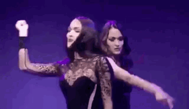 two women are dancing on a stage with purple lights .