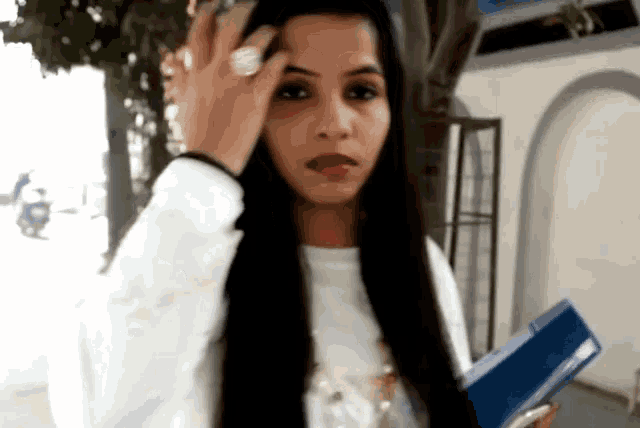 a woman with long black hair is wearing a ring and holding a book