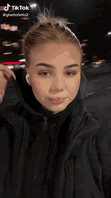 a woman wearing a black jacket and ear buds has a tiktok on her face