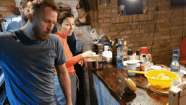 a man in a blue shirt is standing next to a woman in a kitchen preparing food