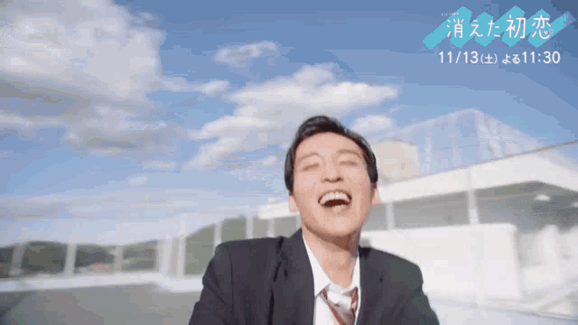 a man in a suit and tie laughs in front of a blue sky with the date 11/13