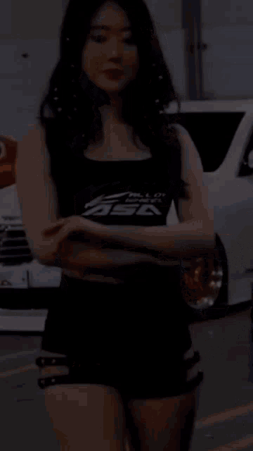 a woman in a black tank top and black shorts is standing in front of a car .