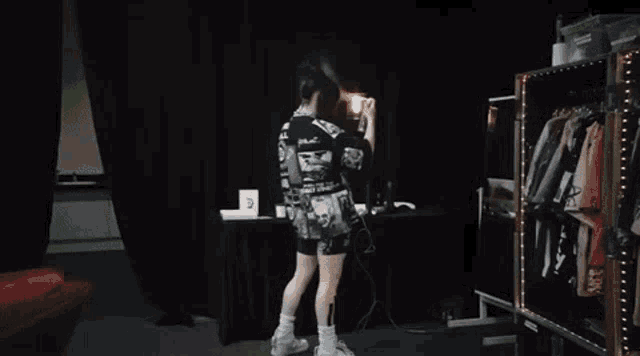 a woman is smoking a cigarette in a dark room while wearing a black shirt and shorts .