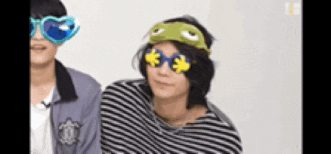 a man wearing a frog mask and sunglasses is sitting next to another man wearing a striped shirt .