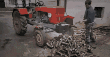 a man is standing next to a pile of wood and a red tractor