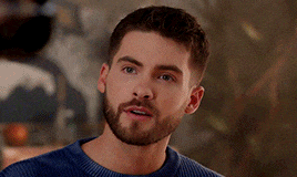 a young man with a beard is wearing a blue sweater and looking at the camera .