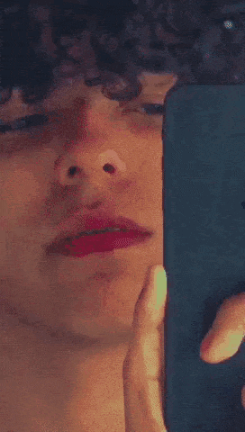 a young man with curly hair is taking a selfie with his phone .