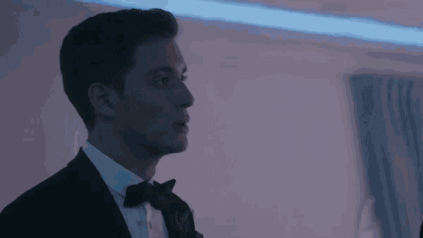 a young man in a tuxedo and bow tie is standing in a dark room .