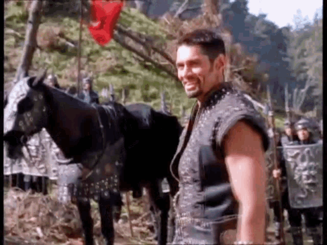 a man is standing next to a black horse in a forest .
