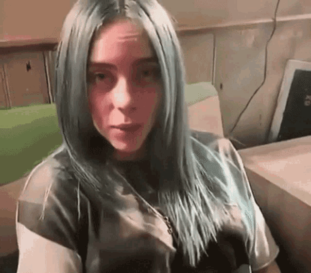 billie eilish with blue hair is sitting in a chair .