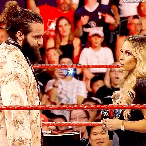 a man and a woman are standing in a wrestling ring with a crowd behind them .