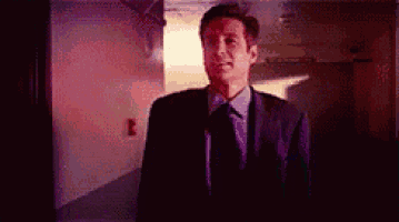 a man in a suit and tie is standing in a hallway with a red light behind him .