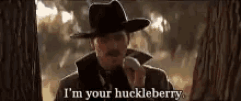 a man in a hat is talking on a cell phone and says i 'm your huckleberry .