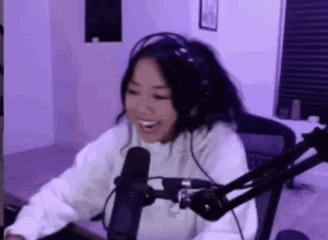 a woman is smiling while sitting in front of a microphone in a room .
