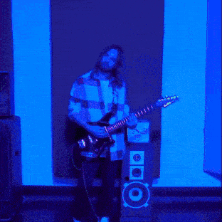 a man with long hair is playing a guitar in front of a speaker