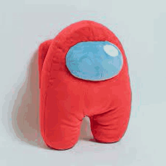a red among us stuffed animal with a blue head is sitting on a white surface .