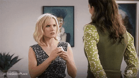 two women are standing next to each other in a living room talking .