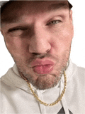 a man wearing a hat and a gold chain is making a face .