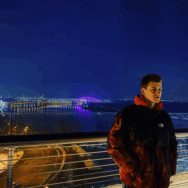 a man wearing a north face jacket stands on a balcony overlooking a bridge